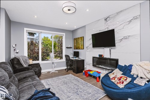 Spacious living area featuring a large window, contemporary wall-mounted electric fireplace, wood-finish flooring, and recessed ceiling lighting - 11305 79 Avenue Nw, Edmonton, AB - Indoor Photo Showing Living Room