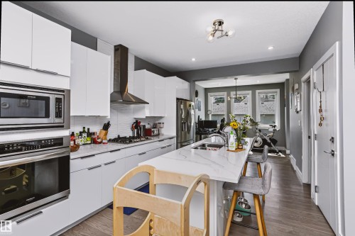 Modern kitchen featuring white flat-panel cabinetry, stainless steel appliances, a white tile backsplash, and an extended island with a built-in sink and seating - 11305 79 Avenue Nw, Edmonton, AB - Indoor Photo Showing Kitchen