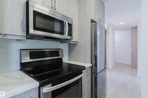 Kitchen featuring stainless steel appliances including an oven range and microwave, light wood-finish cabinetry, light-colored countertops, and a tile backsplash - #303 10883 Saskatchewan Dr Nw, Edmonton, AB - Indoor Photo Showing Kitchen