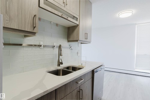 Modern kitchen showcasing light wood-finish cabinetry, white solid surface countertops, and a double basin stainless steel sink with a gooseneck faucet - #303 10883 Saskatchewan Dr Nw, Edmonton, AB - Indoor Photo Showing Kitchen With Double Sink
