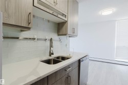 Modern kitchen showcasing light wood-finish cabinetry, white solid surface countertops, and a double basin stainless steel sink with a gooseneck faucet - 