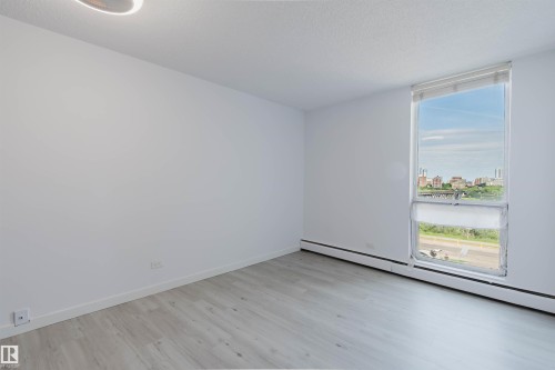 Bright room featuring a large vertical window with roller shades, light wood-finish flooring, white baseboards, and a contemporary flush-mount ceiling light - #303 10883 Saskatchewan Dr Nw, Edmonton, AB - Indoor Photo Showing Other Room