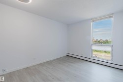 Bright room featuring a large vertical window with roller shades, light wood-finish flooring, white baseboards, and a contemporary flush-mount ceiling light - 