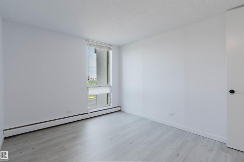 Bright room featuring a large window, light-toned wood-finish flooring, white walls, and a white door with a black knob - #303 10883 Saskatchewan Dr Nw, Edmonton, AB - Indoor Photo Showing Other Room