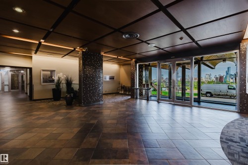 Spacious entryway featuring large format tile flooring, a coffered ceiling with recessed lighting, and expansive glass doors opening to a city skyline - #303 10883 Saskatchewan Dr Nw, Edmonton, AB - Indoor Photo Showing Other Room