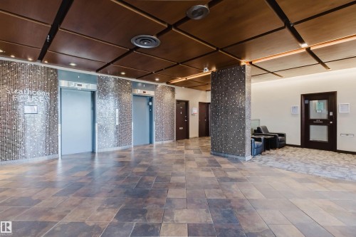 Spacious lobby featuring large format floor tiles, an elevator bank with textured wall finishes, and a wood-panel ceiling with integrated lighting - #303 10883 Saskatchewan Dr Nw, Edmonton, AB - Indoor Photo Showing Other Room