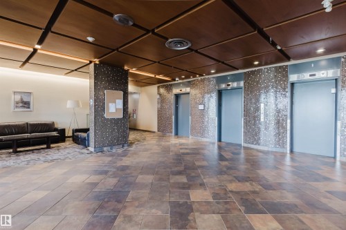 Spacious lobby featuring large format floor tiling, a wood-panel ceiling with integrated lighting, and multiple elevator access points - #303 10883 Saskatchewan Dr Nw, Edmonton, AB - Indoor