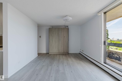Light wood-finish flooring complements the neutral wall color of this spacious interior, featuring a built-in cabinet and sliding glass door with balcony access - #303 10883 Saskatchewan Dr Nw, Edmonton, AB - Indoor Photo Showing Other Room
