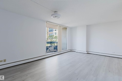 Spacious room featuring light wood-finish flooring, white walls, and a large window with roller shades - #303 10883 Saskatchewan Dr Nw, Edmonton, AB - Indoor Photo Showing Other Room