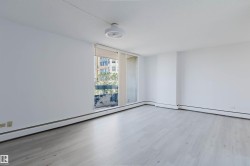 Spacious room featuring light wood-finish flooring, white walls, and a large window with roller shades - 