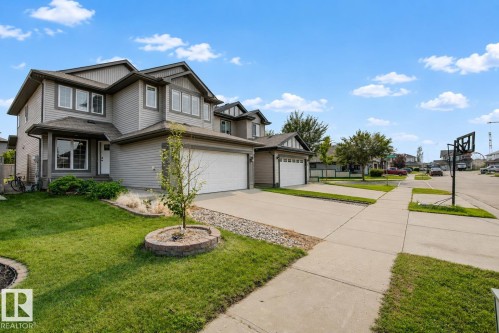 Two-story grey siding residence featuring an attached double garage with white doors, multiple large windows with white trim, and a concrete driveway - 5 Cypress Link, Fort Saskatchewan, AB - Outdoor With Facade
