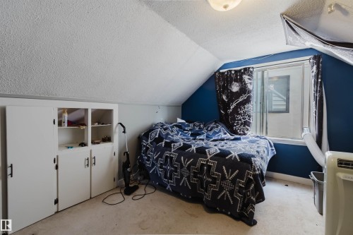 Slanted ceiling room featuring a window with a dark blue accent wall, light-colored carpet, and built-in white cabinetry with black hardware - 10955 72 Avenue Nw, Edmonton, AB - Indoor Photo Showing Bedroom