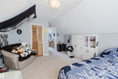 Carpeted room featuring sloped ceilings, light blue wall paint, a natural wood bi-fold door, and built-in white cabinetry with open shelving - 10955 72 Avenue Nw, Edmonton, AB - Indoor Photo Showing Bedroom