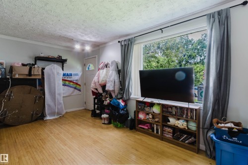 Sunlit room featuring wood-finish flooring, a large picture window, and a white paneled door - 10955 72 Avenue Nw, Edmonton, AB - Indoor