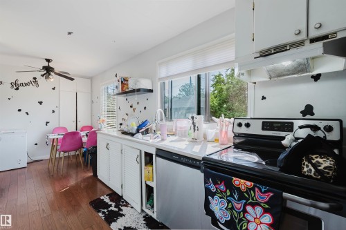 Kitchen featuring wood-finish flooring, white cabinetry, a built-in electric range, and a window with horizontal blinds - 10955 72 Avenue Nw, Edmonton, AB - Indoor Photo Showing Kitchen