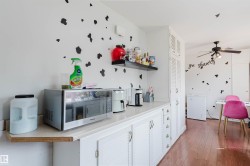 Kitchen area featuring white cabinetry with louvered doors, light-toned countertops, and a dark floating shelf - 