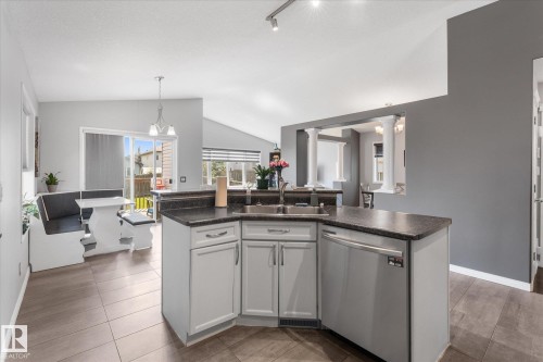 Kitchen featuring light gray cabinetry, dark countertop, stainless steel sink, and integrated dishwasher - 4009 158 Avenue Nw, Edmonton, AB - Indoor Photo Showing Kitchen