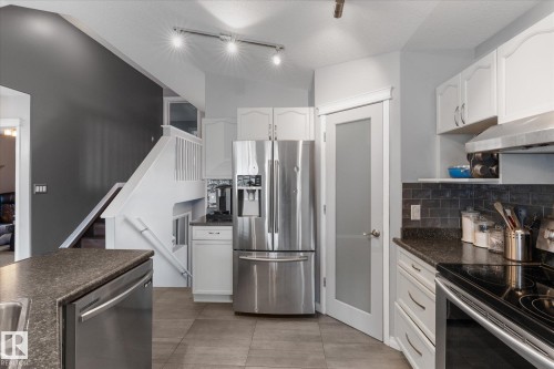 Open-concept kitchen featuring stainless steel appliances, dark stone countertops, subway tile backsplash, white cabinetry, and ceramic tile flooring - 4009 158 Avenue Nw, Edmonton, AB - Indoor Photo Showing Kitchen