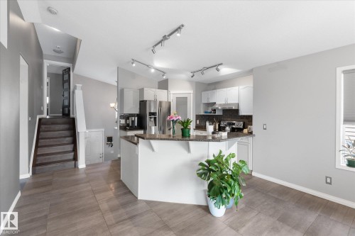 Open-concept main living area featuring a kitchen with a peninsula island, white cabinetry, and stainless steel appliances - 4009 158 Avenue Nw, Edmonton, AB - Indoor Photo Showing Kitchen With Upgraded Kitchen