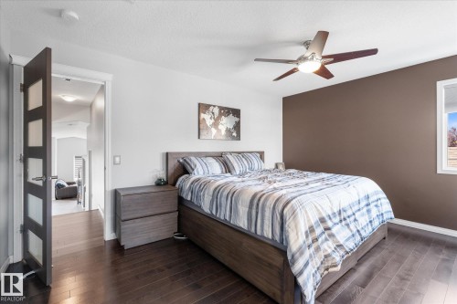 Bedroom featuring dark wood-finish flooring, a contemporary ceiling fan with integrated lighting, a contrasting accent wall, and a large window providing natural light - 4009 158 Avenue Nw, Edmonton, AB - Indoor Photo Showing Bedroom