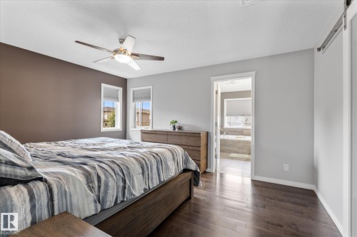 Bedroom featuring wood-finish flooring, a ceiling fan with integrated lighting, two windows with roller shades, and a sliding barn door - 4009 158 Avenue Nw, Edmonton, AB - Indoor Photo Showing Bedroom
