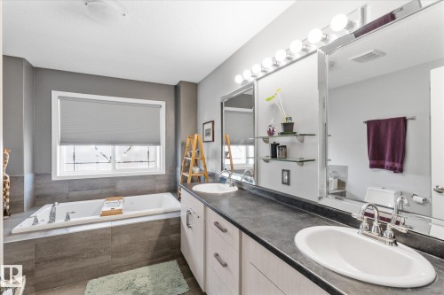 Bathroom featuring a built-in soaking tub with gray tile surround, dual vanity with undermount sinks, and an expansive mirror with integrated lighting - 4009 158 Avenue Nw, Edmonton, AB - Indoor Photo Showing Bathroom