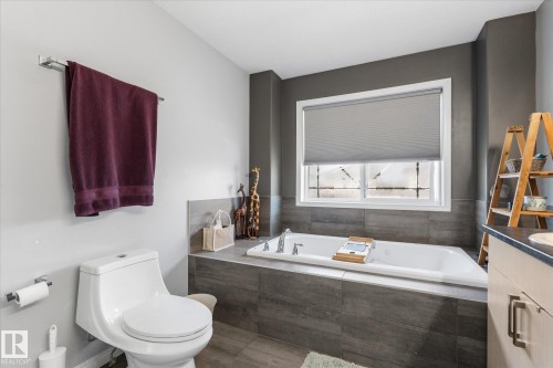 Soaking tub with a tiled surround, complemented by a large window with a privacy blind and a two-tone wall treatment - 4009 158 Avenue Nw, Edmonton, AB - Indoor Photo Showing Bathroom