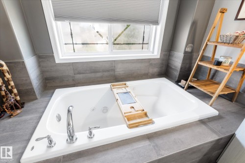 Soaking tub with chrome fixtures, surrounded by gray tile flooring and wall accents - 4009 158 Avenue Nw, Edmonton, AB - Indoor Photo Showing Bathroom