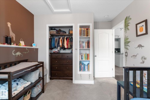 Plush carpeted bedroom featuring a built-in bookshelf, a recessed closet with wood-finish dresser, and a white interior door - 4009 158 Avenue Nw, Edmonton, AB - Indoor