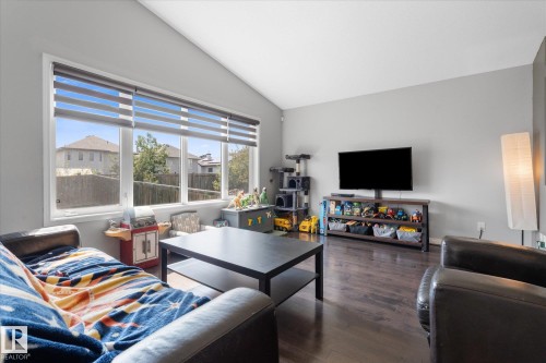 Spacious living area featuring a vaulted ceiling, wood-finish flooring, and a large multi-pane window with horizontal blinds - 4009 158 Avenue Nw, Edmonton, AB - Indoor Photo Showing Living Room
