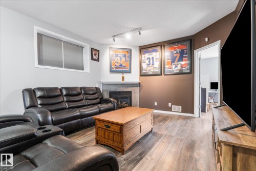 Spacious room featuring wood-finish flooring, a contemporary fireplace with a tile surround, and a corner-mounted spotlight fixture - 4009 158 Avenue Nw, Edmonton, AB - Indoor Photo Showing Living Room With Fireplace