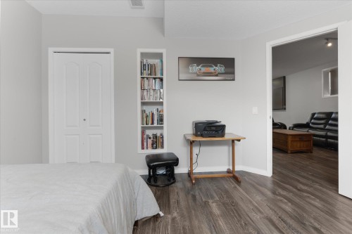 Room featuring light gray walls, wood-finish flooring, a white bi-fold closet door, and a built-in vertical bookshelf - 4009 158 Avenue Nw, Edmonton, AB - Indoor Photo Showing Bedroom