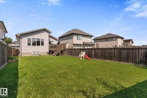 Expansive fenced backyard featuring a substantial lawn area and a two-story residence with a wood-finish deck and stairs - 4009 158 Avenue Nw, Edmonton, AB - Outdoor With Backyard With Exterior