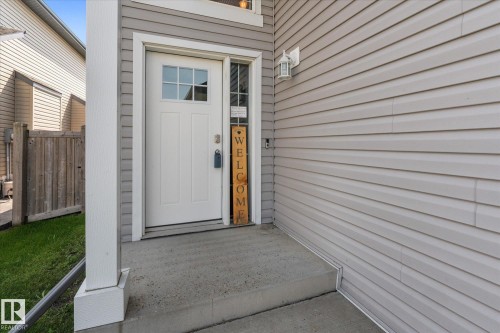 Entryway featuring a white door with upper window panes, gray horizontal siding, an exterior light fixture, and a concrete porch with steps - 4009 158 Avenue Nw, Edmonton, AB - Outdoor With Exterior