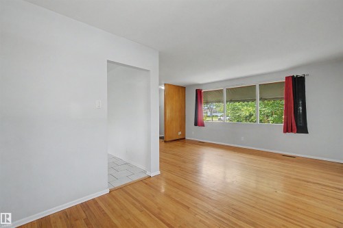 Spacious room featuring hardwood flooring, multiple windows providing natural illumination, light gray wall finishes, and a wood-paneled accent wall - 8215 149 Street Nw, Edmonton, AB - Indoor Photo Showing Other Room