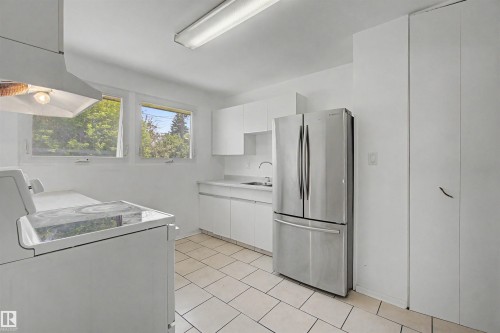 Contemporary kitchen featuring a stainless steel French door refrigerator, white cabinetry, a ceramic cooktop range, a built-in exhaust hood, and white tile flooring - 8215 149 Street Nw, Edmonton, AB - Indoor Photo Showing Laundry Room
