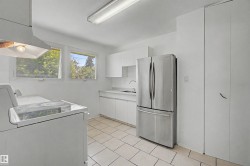 Contemporary kitchen featuring a stainless steel French door refrigerator, white cabinetry, a ceramic cooktop range, a built-in exhaust hood, and white tile flooring - 