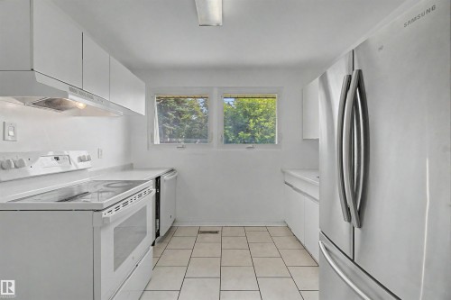 Kitchen featuring white cabinetry, white solid surface countertops, white tile flooring, white electric range, and a stainless steel refrigerator - 8215 149 Street Nw, Edmonton, AB - Indoor Photo Showing Laundry Room
