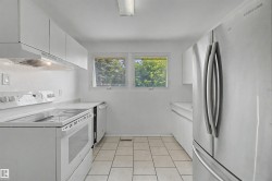 Kitchen featuring white cabinetry, white solid surface countertops, white tile flooring, white electric range, and a stainless steel refrigerator - 