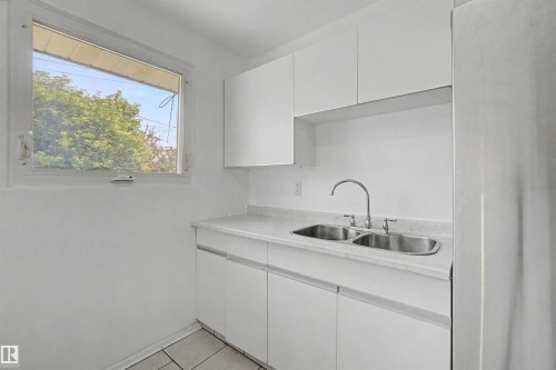 Kitchen featuring white cabinetry, light-colored countertops, a double basin stainless steel sink with a gooseneck faucet, and a window - 8215 149 Street Nw, Edmonton, AB - Indoor Photo Showing Kitchen With Double Sink