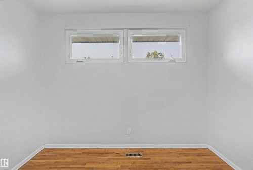 Bright room featuring wood-finish flooring, white painted walls, and two horizontal windows - 8215 149 Street Nw, Edmonton, AB - Indoor Photo Showing Other Room
