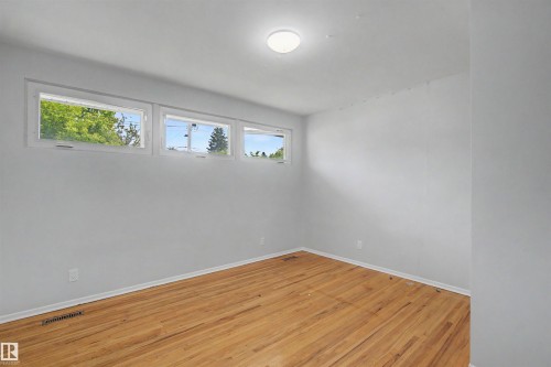 Room featuring three horizontal transom windows, wood-finish flooring, white baseboards, and a flush-mount ceiling light fixture - 8215 149 Street Nw, Edmonton, AB - Indoor Photo Showing Other Room