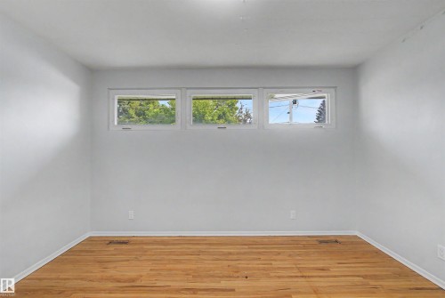 Hardwood flooring throughout a room featuring light-colored walls and a trio of horizontal windows - 8215 149 Street Nw, Edmonton, AB - Indoor Photo Showing Other Room