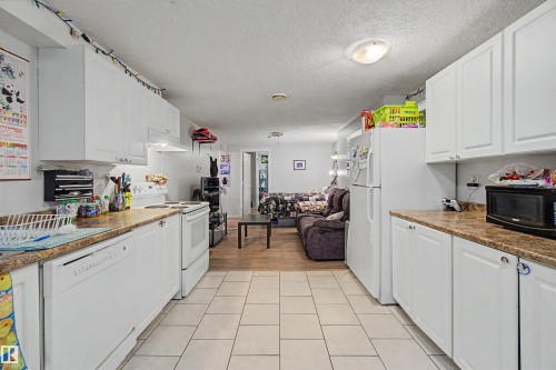 Kitchen featuring white cabinetry, stone-finish countertops, white appliances, and light-toned tile flooring - 8215 149 Street Nw, Edmonton, AB - Indoor Photo Showing Kitchen