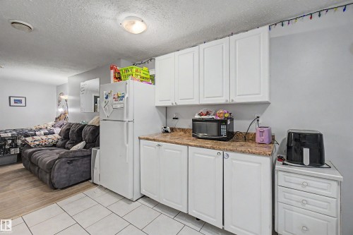 Compact kitchen area featuring white cabinetry, light-toned countertops, and a full-size refrigerator - 8215 149 Street Nw, Edmonton, AB - Indoor Photo Showing Kitchen