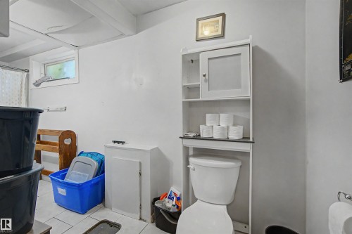Bathroom featuring white walls, exposed ceiling beams, a white toilet with an over-the-toilet storage cabinet, and a window with natural light - 8215 149 Street Nw, Edmonton, AB - Indoor
