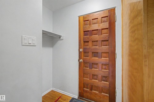 Solid wood entry door with square panel design, wood-finish flooring, and integrated coat closet with shelf and hanging rod - 8215 149 Street Nw, Edmonton, AB - Indoor