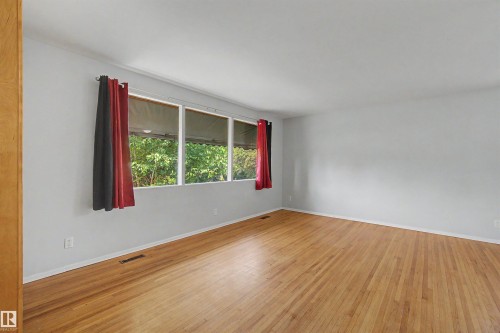 Spacious room featuring wood-finish flooring, light grey walls, and a large window array with white trim - 8215 149 Street Nw, Edmonton, AB - Indoor Photo Showing Other Room