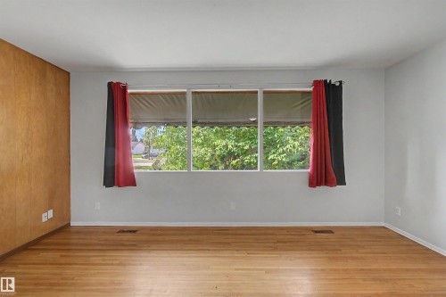 Spacious interior featuring a large multi-pane window, wood-finish flooring, a wood-paneled accent wall, and light gray painted walls - 8215 149 Street Nw, Edmonton, AB - Indoor Photo Showing Other Room