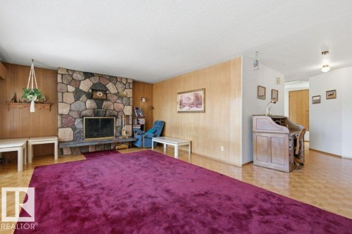 Stone-clad fireplace with hearth, wood paneling, parquet wood-finish flooring, and built-in shelving - 10459 66 Avenue Nw, Edmonton, AB - Indoor Photo Showing Living Room With Fireplace
